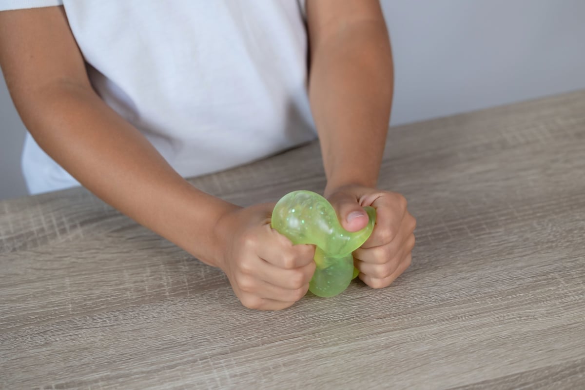 Child's hands squeezing a translucent green stress squishy on a wooden table